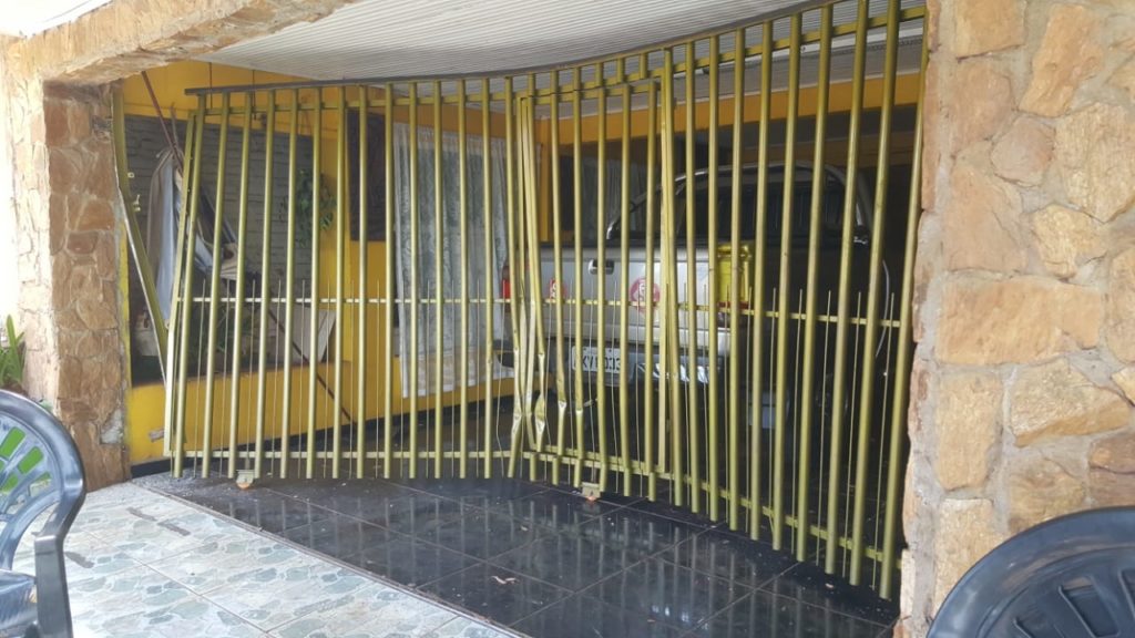 Mulher retira carro da garagem, atravessa rua, atinge árvore e portão de residência