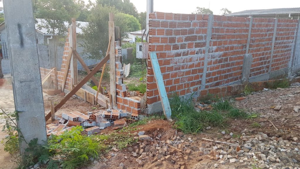 Recolhendo caçamba de entulhos, motorista derruba parte de muro de imóvel no Bairro Neva