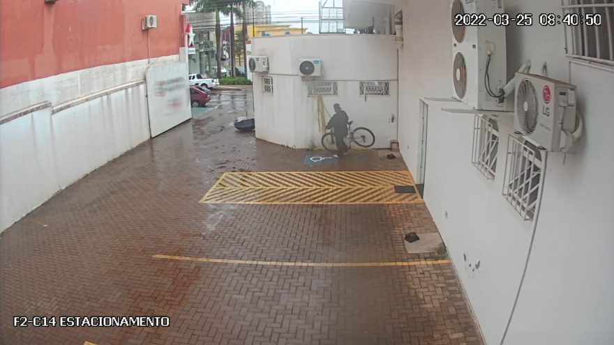 Com todo cuidado, homem leva bicicleta que estava parada em estacionamento de farmácia