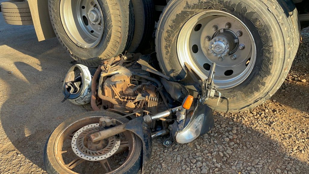 Moto fica presa em rodado de caminhão após colisão; piloto é levado ao hospital